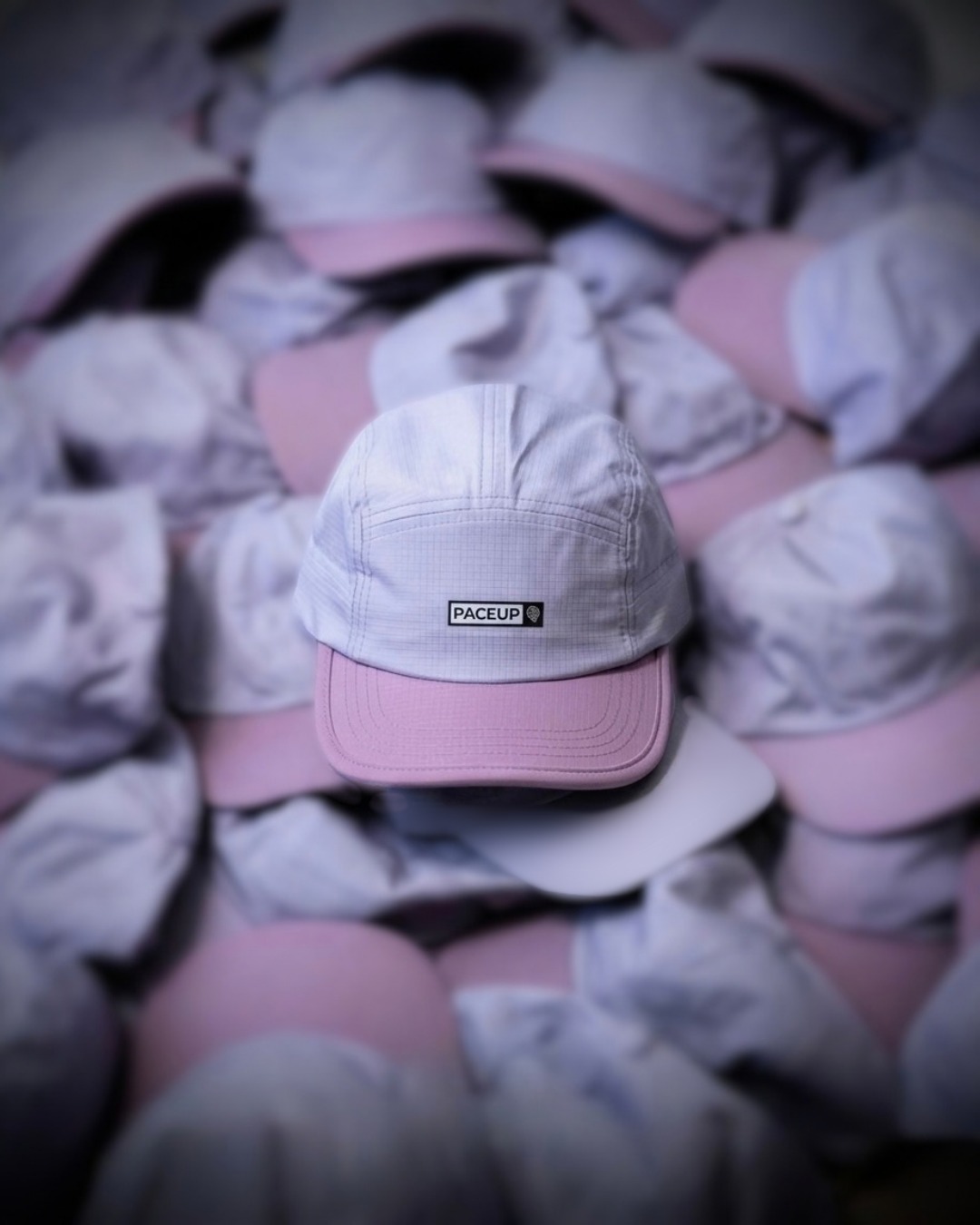 Gorra Paceup lila con visera rosa sobre una pila de gorras